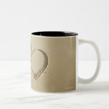 Two overlying hearts drawn on the beach with mug