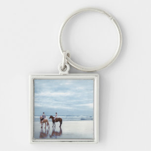 A couple riding horses on Parkiri beach in New Key Ring