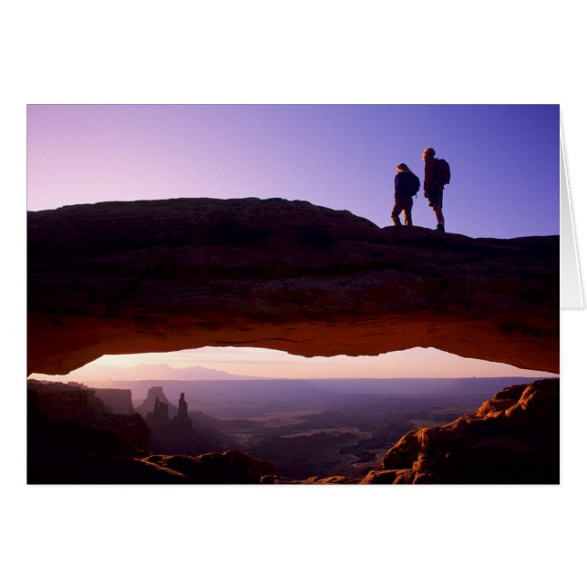 A couple watches sunrise from atop Mesa Arch in (Front Horizontal)