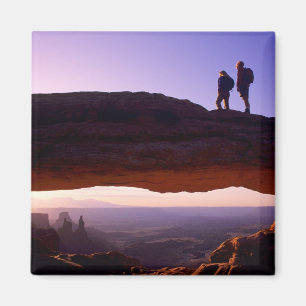 A couple watches sunrise from atop Mesa Arch in Magnet