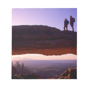 A couple watches sunrise from atop Mesa Arch in Notepad