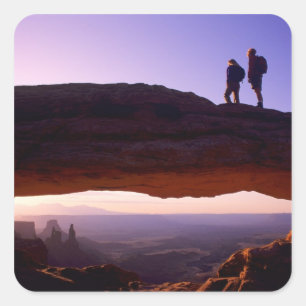 A couple watches sunrise from atop Mesa Arch in Square Sticker