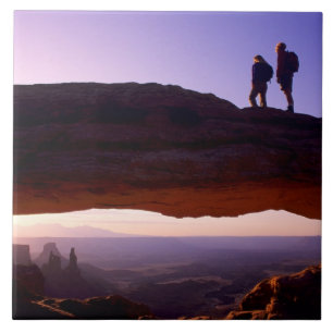 A couple watches sunrise from atop Mesa Arch in Tile
