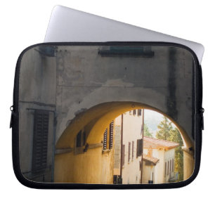 A person walking under an arch, down a hill in laptop sleeve