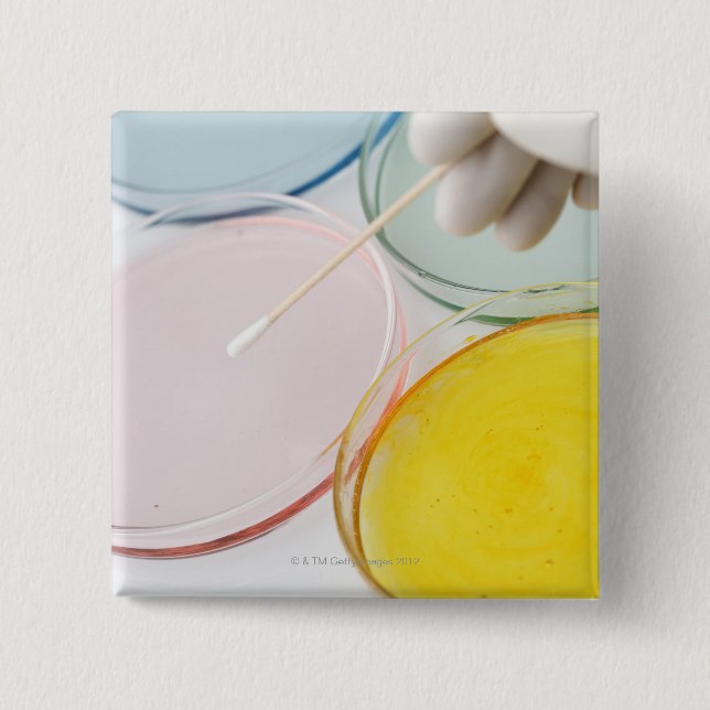 A plastic gloved hand sampling from petrie 15 cm square badge (Front)