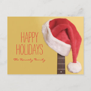 A Santa hat hangs on an acoustic guitar in front Holiday Postcard