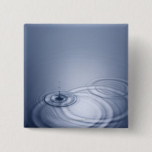A single droplet of water falling into a calm 15 cm square badge