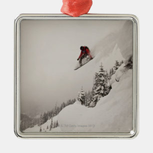 A snowboarder jumps off a cliff into powder in metal tree decoration
