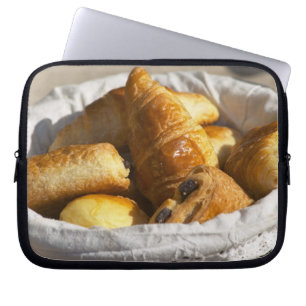 A wicker breakfast basket with croissants, and laptop sleeve