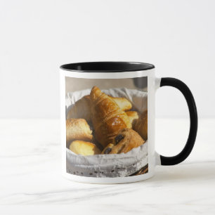 A wicker breakfast basket with croissants, and mug
