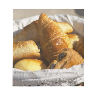 A wicker breakfast basket with croissants, and notepad
