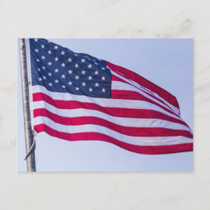 American flag flying high against a light blue sky postcard