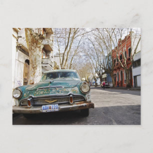 An old car rusty and flaky colour parked in the postcard