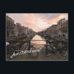 Bicycles at sunset in Amsterdam Postcard<br><div class="desc">Postcard of some bicycles locked to the bar of a bridge over Prinsengracht canal lined by traditional canal houses at sunset in the city center of Amsterdam in the Netherlands with the text 'Amsterdam!'.</div>