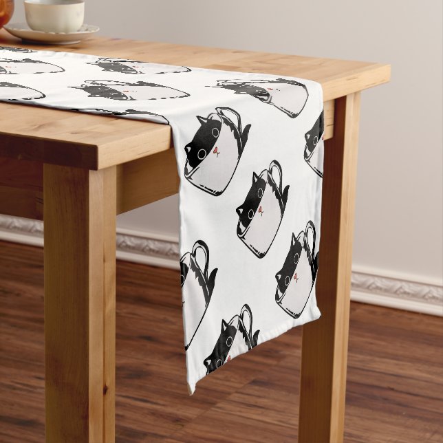 Black kitten with red nose hiding in a cup short table runner (In Situ)
