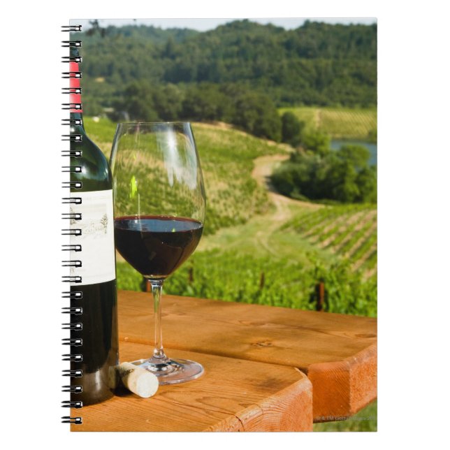 Bottle of red wine and glass on table notebook (Front)