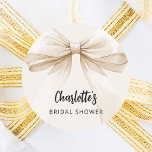 Bow beige cream Bridal Shower Classic Round Sticker<br><div class="desc">A beige,  cream coloured background. Decorated with a large bow.  Personalise and add the bride's name. Black handwritten style script.</div>