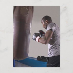 Boxer using punching bag in gym postcard
