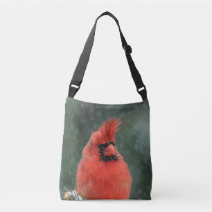 Cardinal in a pine tree during a snow storm crossbody bag