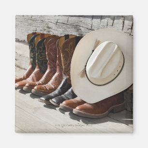 Cowboy hat on row of cowboy boots outside a log magnet