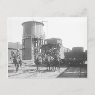 Cowboys on horses posing in front of a train postcard