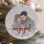 First Christmas Engaged Photo Red Script Ceramic Ornament<br><div class="desc">Commemorate your engagement with this beautiful modern keepsake ornament. The burgundy red text reads "Our first Christmas engaged, " with the word "engaged" in bold handwriting script with flourishes before and after. Replace the sample image with your favourite photo, and add your names and the year. A white gradient filter...</div>