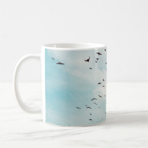 Flock of grey dove fly on vintage blue sky. above, coffee mug