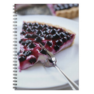 Fork slicing blueberry pie on plate notebook