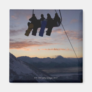 Four snowboarders are silhouetted on a ski lift magnet