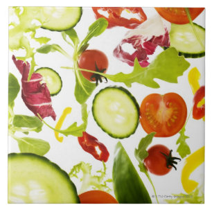 Fresh mixed salad vegetables falling to camera ceramic tile