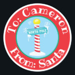 From Santa Sticker Custom Name North Pole Sign<br><div class="desc">This custom sticker label features a festive Christmas theme that is perfect for labelling your gifts. A North Pole sign is pictured in the centre beneath falling snow. A sample name is printed across the top, over a red banner. You can personalise the sticker to include your own custom name...</div>