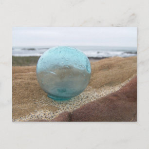 Glass float on sand at beach postcard