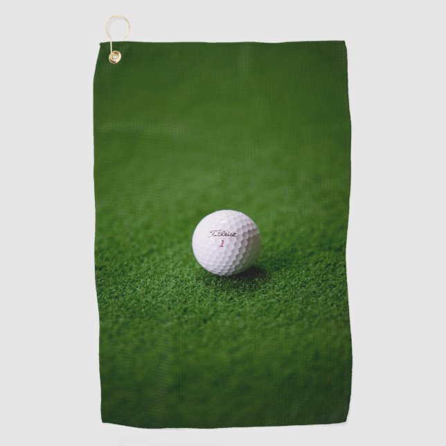 Golf ball on a green surface Golf Towels (Front)