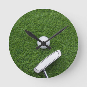 Golf ball with putter are on green grass round clock