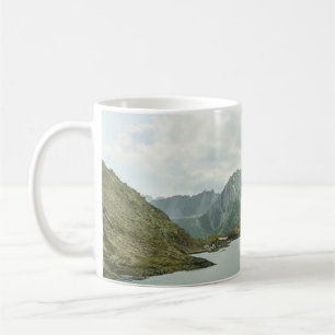 GREEN AND BROWN MOUNTAINS NEAR BODY OF WATER UNDER COFFEE MUG