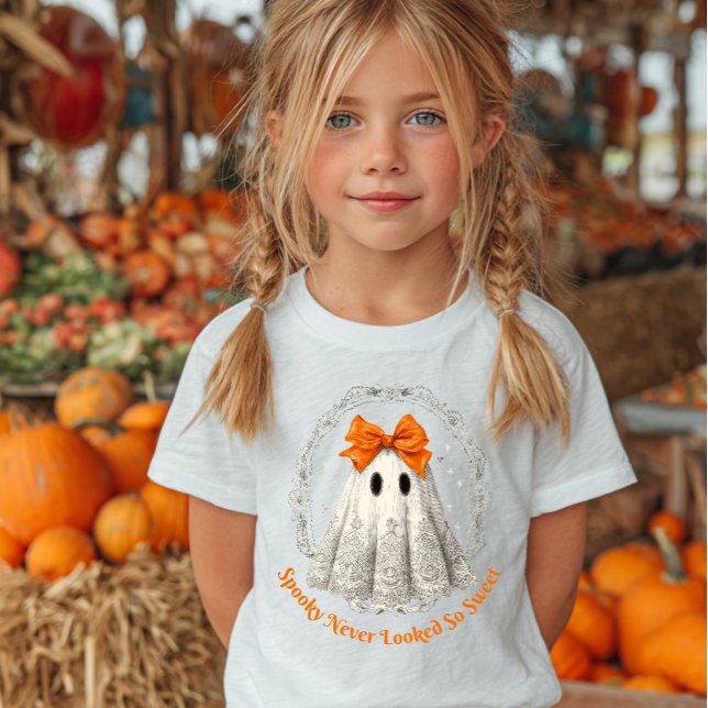 Lace Ghost with Bow in Wreath and Stars Baby T-Shirt (Young girl with blonde pigtails wearing a Halloween-themed T-shirt featuring a cute ghost.)