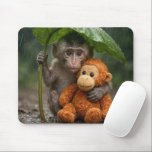 Macaque Monkey with a Stuffed Orangutan Mouse Pad<br><div class="desc">A young macaque monkey uses a large green leaf as a makeshift umbrella while holding onto a stuffed orange orangutan toy in the gentle rain of a lush forest</div>