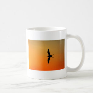Magnificent frigate bird flying orange sunset coffee mug