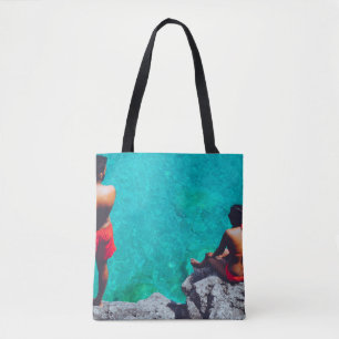 Man and woman sitting on boulder near body of wate tote bag