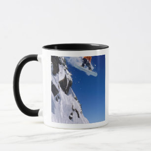 Man on a snowboard jumping off a cornice at mug