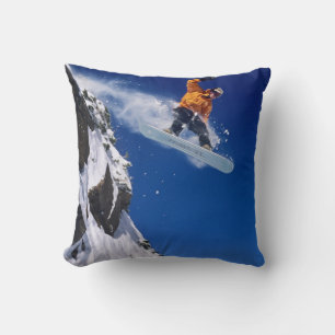 Man on a snowboard jumping off a cornice cushion