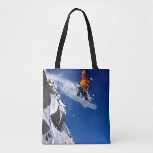 Man on a snowboard jumping off a cornice tote bag