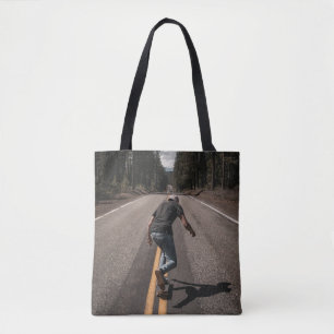 Man playing skateboard on road in the morning tote bag