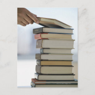 Man's hand taking a book from a stack of books postcard