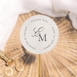 Minimalist Monogram Wedding Thank You Favor Classic Round Sticker<br><div class="desc">A thank you sticker to match our Editorial Photo Wedding collection. The monogram features script calligraphy and a classic serif font in a unique layout. A message of your choice is printed in serif typography around the monogram, creating a circular frame. The background is an off-white ivory color. This favor...</div>