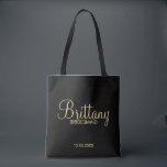Modern Black and Gold Personalised Bridesmaids Tote Bag<br><div class="desc">Modern Black and Gold Personalised Bridesmaids Gifts featuring personalised bridesmaid's name in gold modern script font style with title and wedding date in modern sans serif font style on black background. Also perfect for Maid of Honour, Flower Girl, Mother of the Bride and more. Please Note: The foil details are...</div>