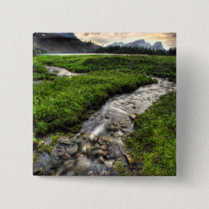 Mountain creek descends through meadow towards 15 cm square badge