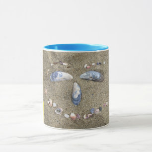 Mug yellow face made in the sand with sea shells