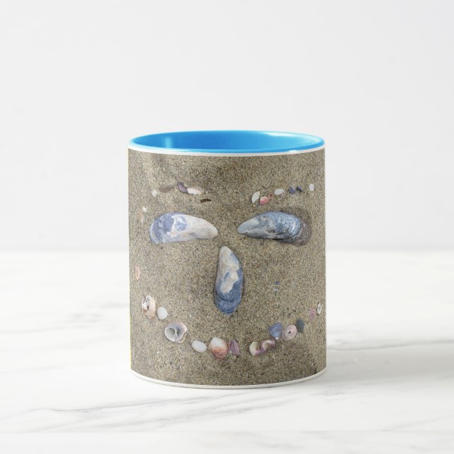Mug yellow face made in the sand with sea shells (Center)