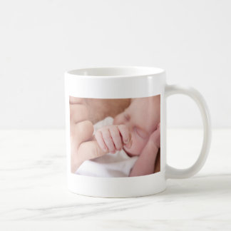 newborn baby holding fathers finger coffee mug